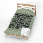 A single wooden toddler bed with a sage green comforter featuring a black printed Christmas-themed parody quote about 'Nutcracker,' shown on a clean white background.