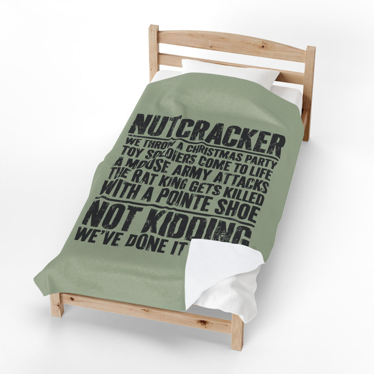 A single wooden toddler bed with a sage green comforter featuring a black printed Christmas-themed parody quote about 'Nutcracker,' shown on a clean white background.