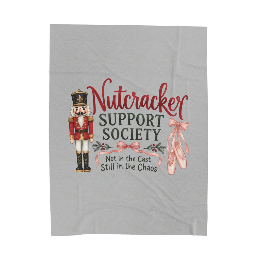 A light gray fabric item, likely a towel or blanket, featuring a Nutcracker-themed graphic print with a nutcracker soldier, ballet slippers, and the text 'Nutcracker SUPPORT SOCIETY Not in the Cast Still in the Chaos'.