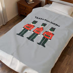 A light gray blanket with a 'TEAM SOLDIERS' graphic featuring three toy soldier illustrations, shown on a bed in a bedroom setting.