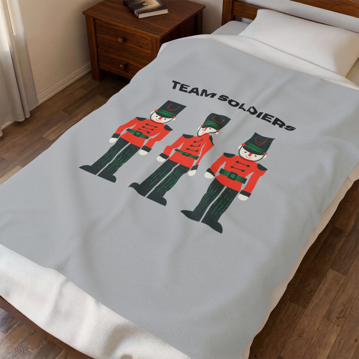 A light gray blanket with a 'TEAM SOLDIERS' graphic featuring three toy soldier illustrations, shown on a bed in a bedroom setting.