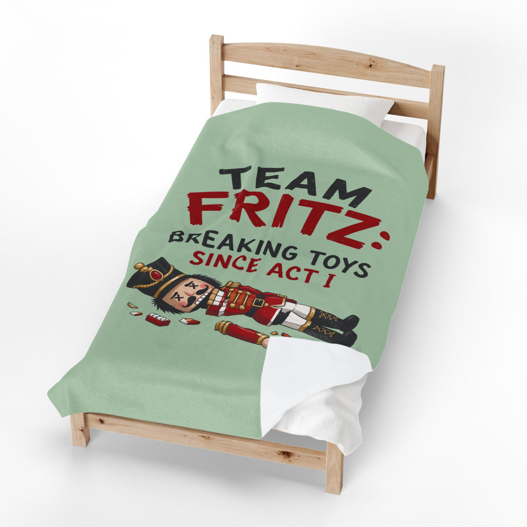 A light green bedding set on a wooden toddler bed, featuring a graphic print of a nutcracker and the text 'TEAM FRITZ: BREAKING TOYS SINCE ACT I'.