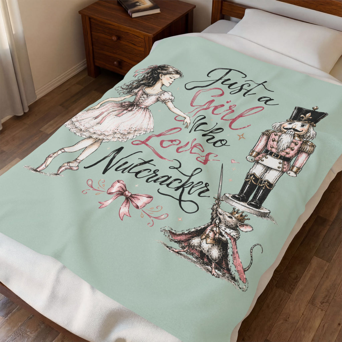 A mint green bedding blanket featuring Alice in Wonderland artwork, including Alice, a nutcracker, a mouse, and the phrase 'Just a Girl who Loves a Nutcracker,' shown on a bed in a bedroom.