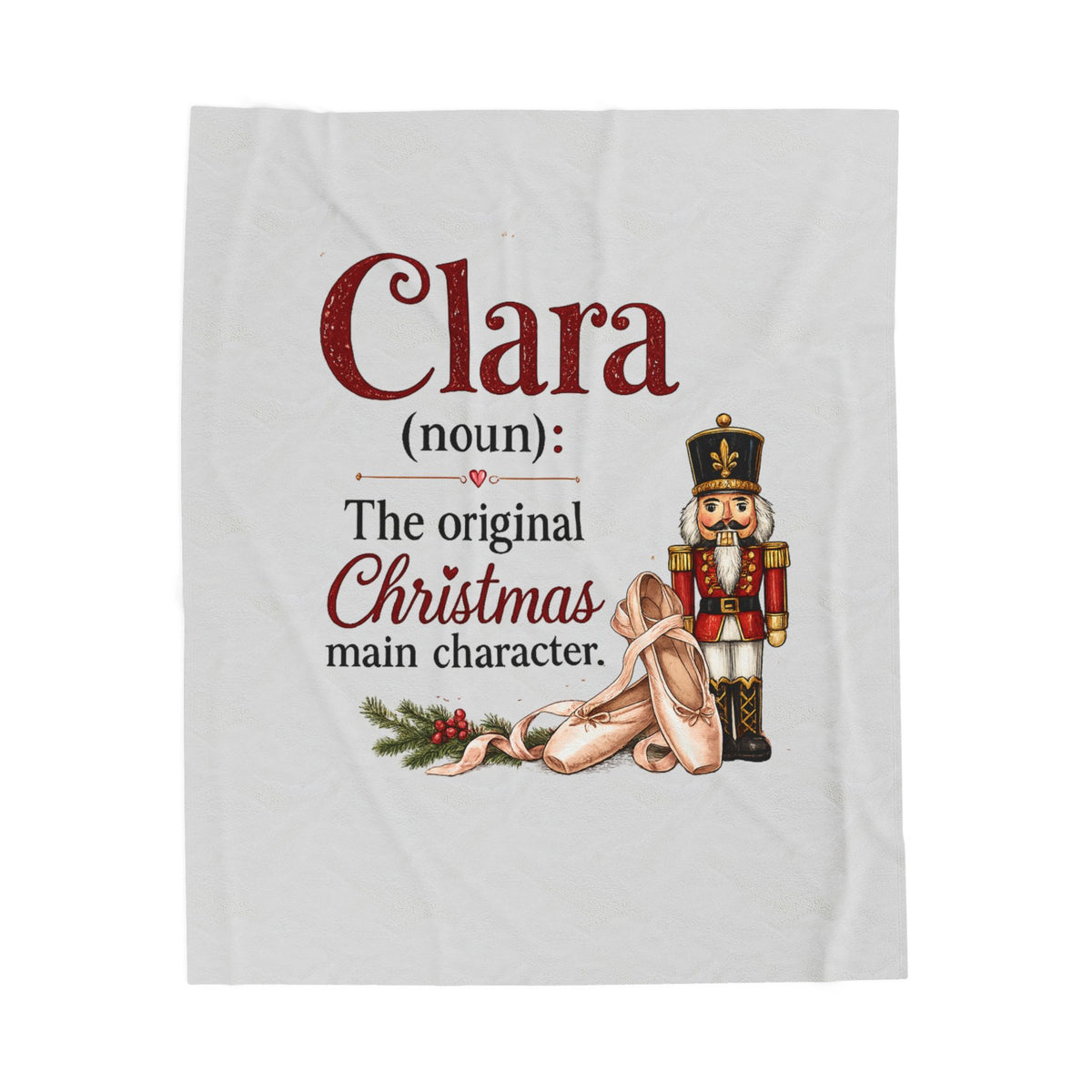 A white fleece blanket featuring a personalized Christmas print with the text 'Clara (noun): The original Christmas main character.' in red and black lettering, accompanied by an illustration of a nutcracker and a pair of tights.