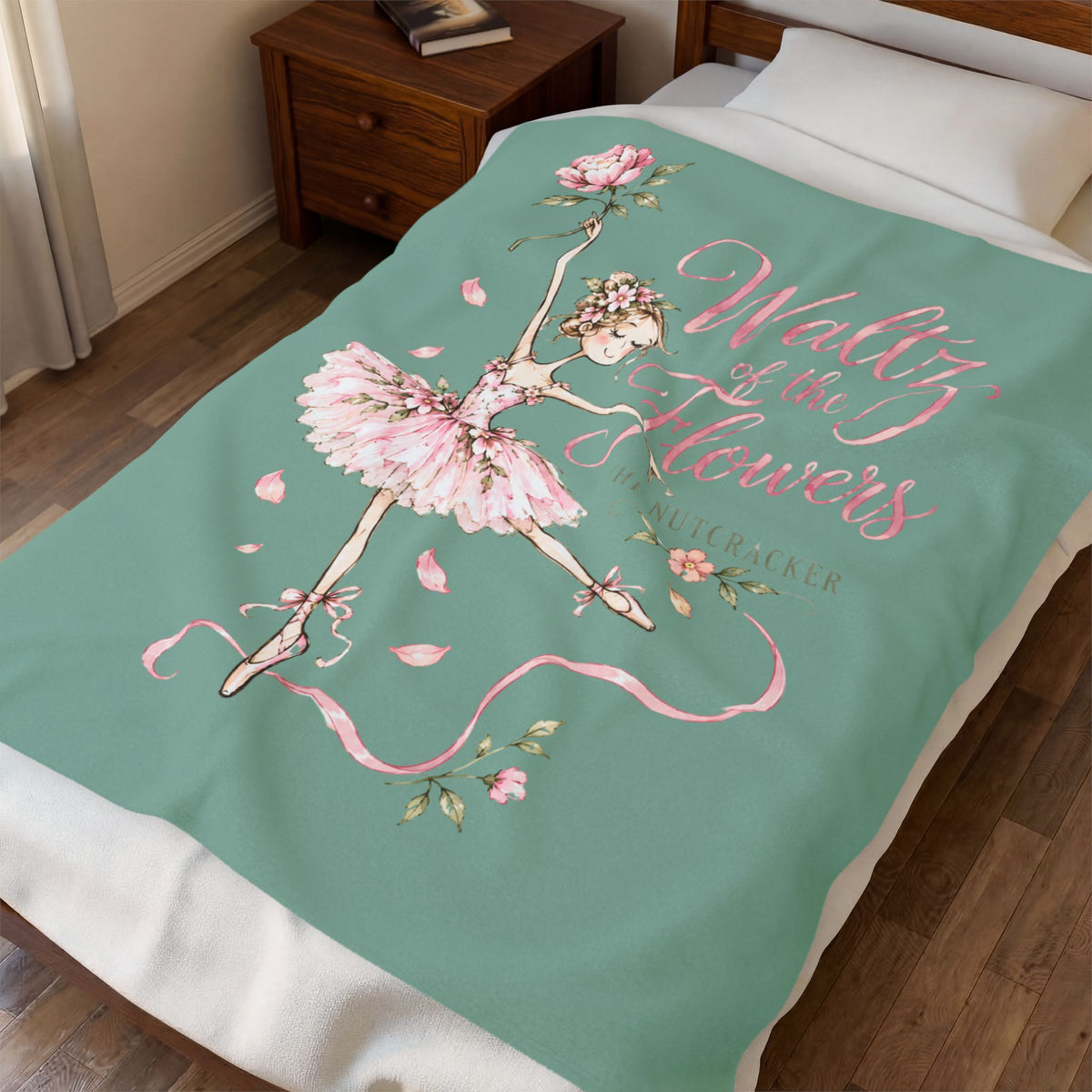 A bedding set on a bed in a bedroom, featuring a mint green blanket with a pink ballerina, roses, and the text 'Waltz of the Flowers' and 'The Nutcracker'.