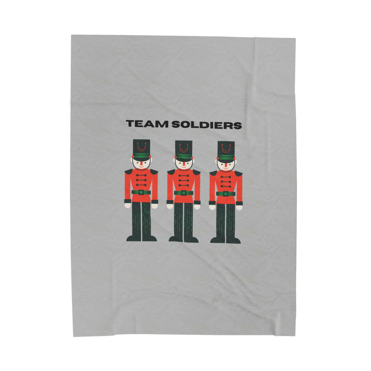 A light gray fabric item, likely a towel or blanket, featuring a graphic print of three toy soldier nutcrackers and the text 'TEAM SOLDIERS' in black.