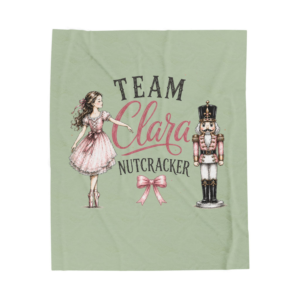 A sage green blanket featuring a custom printed design with the text 'TEAM Clara NUTCRACKER' in black and pink script, accompanied by illustrations of a ballerina girl in a pink dress and a nutcracker.