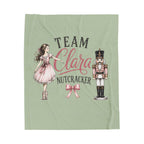 A sage green blanket featuring a custom printed design with the text 'TEAM Clara NUTCRACKER' in black and pink script, accompanied by illustrations of a ballerina girl in a pink dress and a nutcracker.