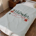 A light blue fleece bedding set, including a duvet cover and matching pillowcase, styled on a bed in a bedroom. The duvet cover features a printed graphic of a nutcracker, a spool of red thread, and the text 'Nutcracker Sewing Club' in green and red.