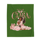 A green blanket featuring a graphic print of a young girl in a pink dress with the text 'TEAM CLARA' above her, accompanied by a gift box.