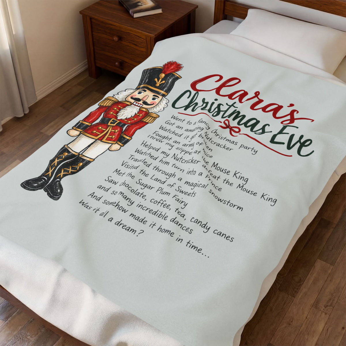 A personalized Christmas blanket laid out on a bed in a bedroom. The blanket is off-white and features a large printed design with a nutcracker illustration, red and green script text reading 'Clara's Christmas Eve,' and a list of holiday song titles in black text.