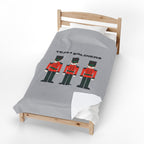 A light gray bedding set on a wooden toddler bed, featuring a graphic print of three toy soldier nutcrackers and the text 'TEAM SOLDIERS'.
