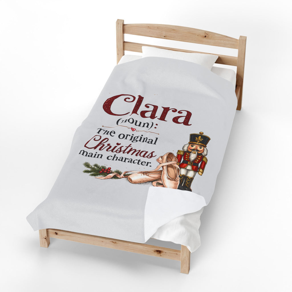 A white personalized Christmas blanket draped over a wooden toddler bed, featuring a printed design with the text 'Clara (Aunt) The original Christmas main character' alongside an illustration of a nutcracker and a ballerina.