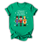 A green short-sleeve t-shirt with a graphic print of three nutcracker figures and the text 'I Paused My Game to be Here' in white, displayed on a clean white background.