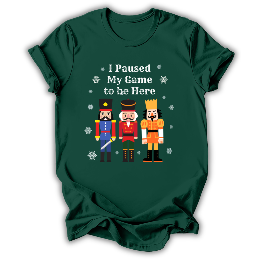 A dark green short-sleeve t-shirt with a graphic print of three nutcracker figures and the text 'I Paused My Game to be Here' in white, displayed on a clean white background.
