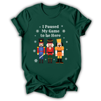 A dark green short-sleeve t-shirt with a graphic print of three nutcracker figures and the text 'I Paused My Game to be Here' in white, displayed on a clean white background.