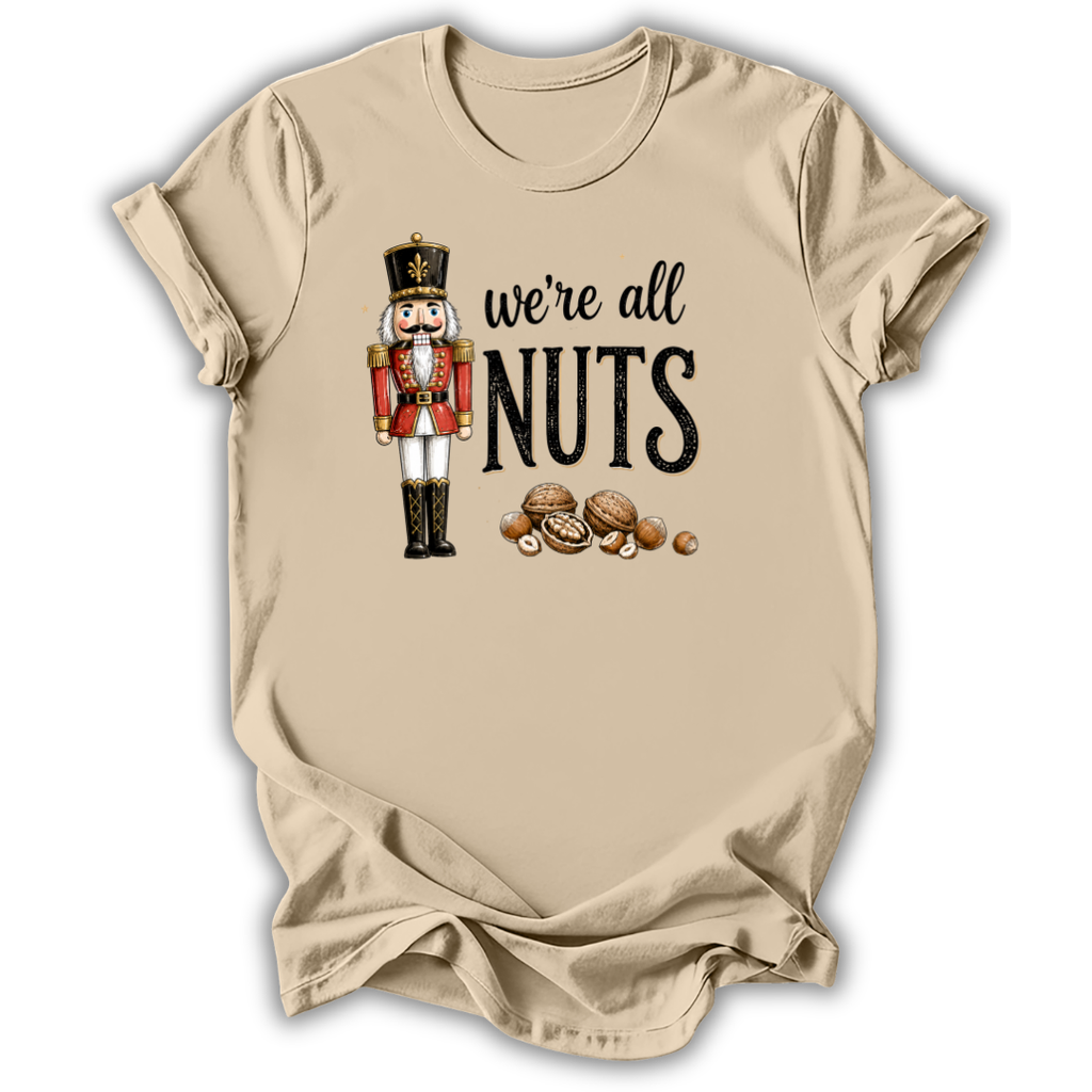 A beige short-sleeve t-shirt with a graphic print of a nutcracker soldier and the text 'we're all NUTS' alongside illustrated walnuts, shown on a plain white background.