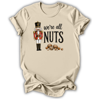 A beige short-sleeve t-shirt with a graphic print of a nutcracker and the text 'we're all NUTS' alongside illustrated walnuts, shown on a white background.