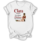 A white short-sleeve t-shirt with a custom printed graphic on the front. The graphic features the text 'Clara (noun): The original Christmas main character.