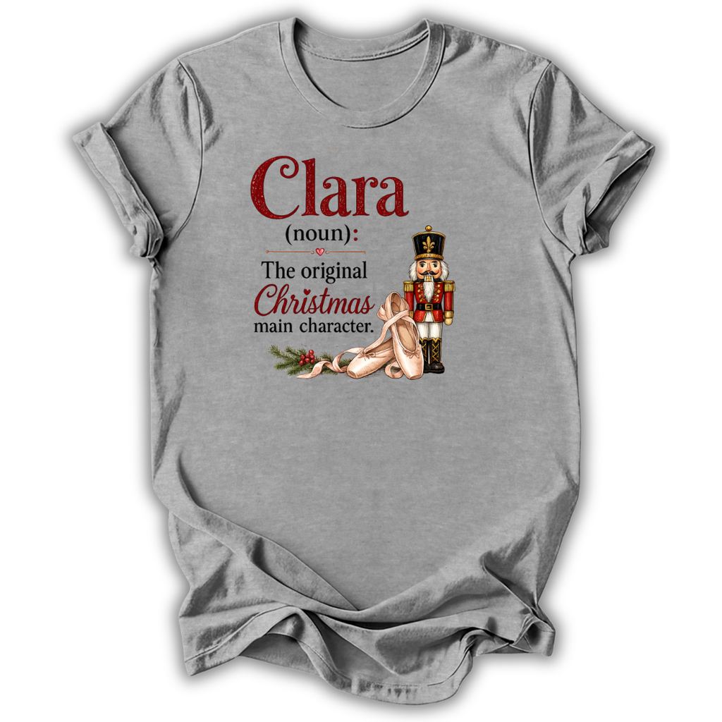 A heather gray short-sleeve t-shirt with a graphic print on the front. The print features the text 'Clara (noun): The original Christmas main character.