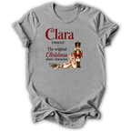 A heather gray short-sleeve t-shirt with a graphic print on the front. The print features the text 'Clara (noun): The original Christmas main character.
