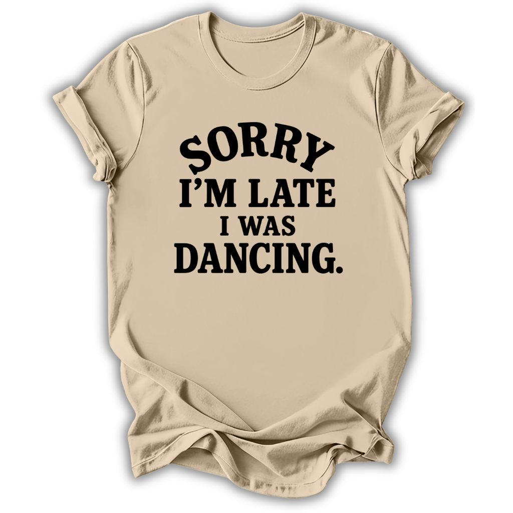 A beige short-sleeve t-shirt with black text reading 'SORRY I'M LATE I WAS DANCING.' printed on the front, shown against a plain white background.