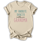 A beige short-sleeve t-shirt with a graphic text print reading 'MY FAVORITE DANCER calls me GRANDMA' in teal, black, and pink lettering, displayed on a clean white background.