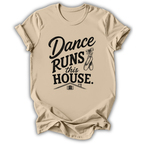 A beige short-sleeve t-shirt with a black graphic print that reads 'Dance Runs This House.' accompanied by ballet shoes and a small house illustration, displayed on a clean white background.