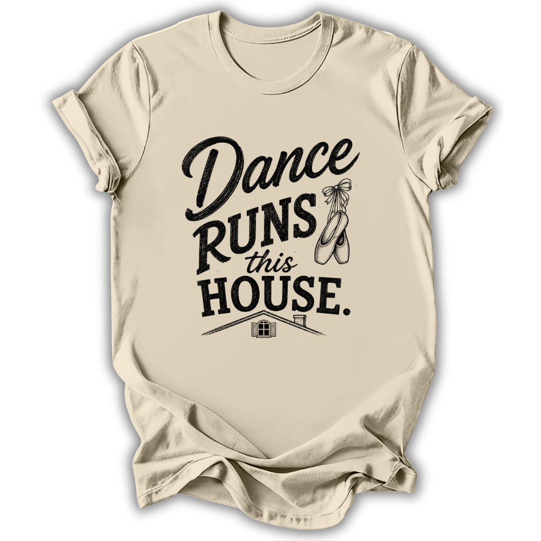 A beige short-sleeve t-shirt with a black graphic print that reads 'Dance Runs This House.' accompanied by a ballet shoe illustration, displayed on a clean white background.