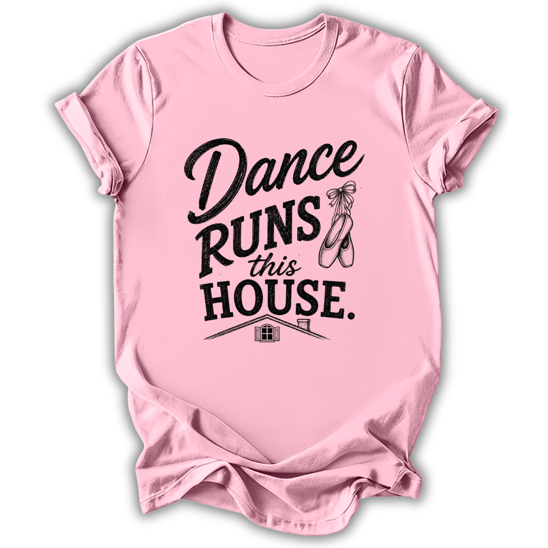 A light pink short-sleeve t-shirt with a black graphic print that reads 'Dance Runs This House.' accompanied by a ballet shoe illustration, shown on a white background with a drop shadow.