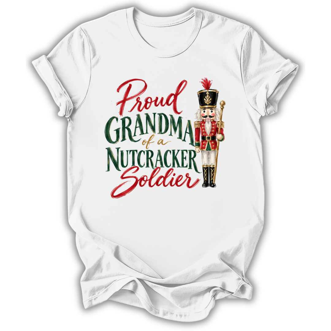 A white short-sleeve crewneck t-shirt with a graphic print that reads 'Proud GRANDMA of a NUTCRACKER Soldier' in red and green lettering, accompanied by an illustration of a nutcracker soldier.
