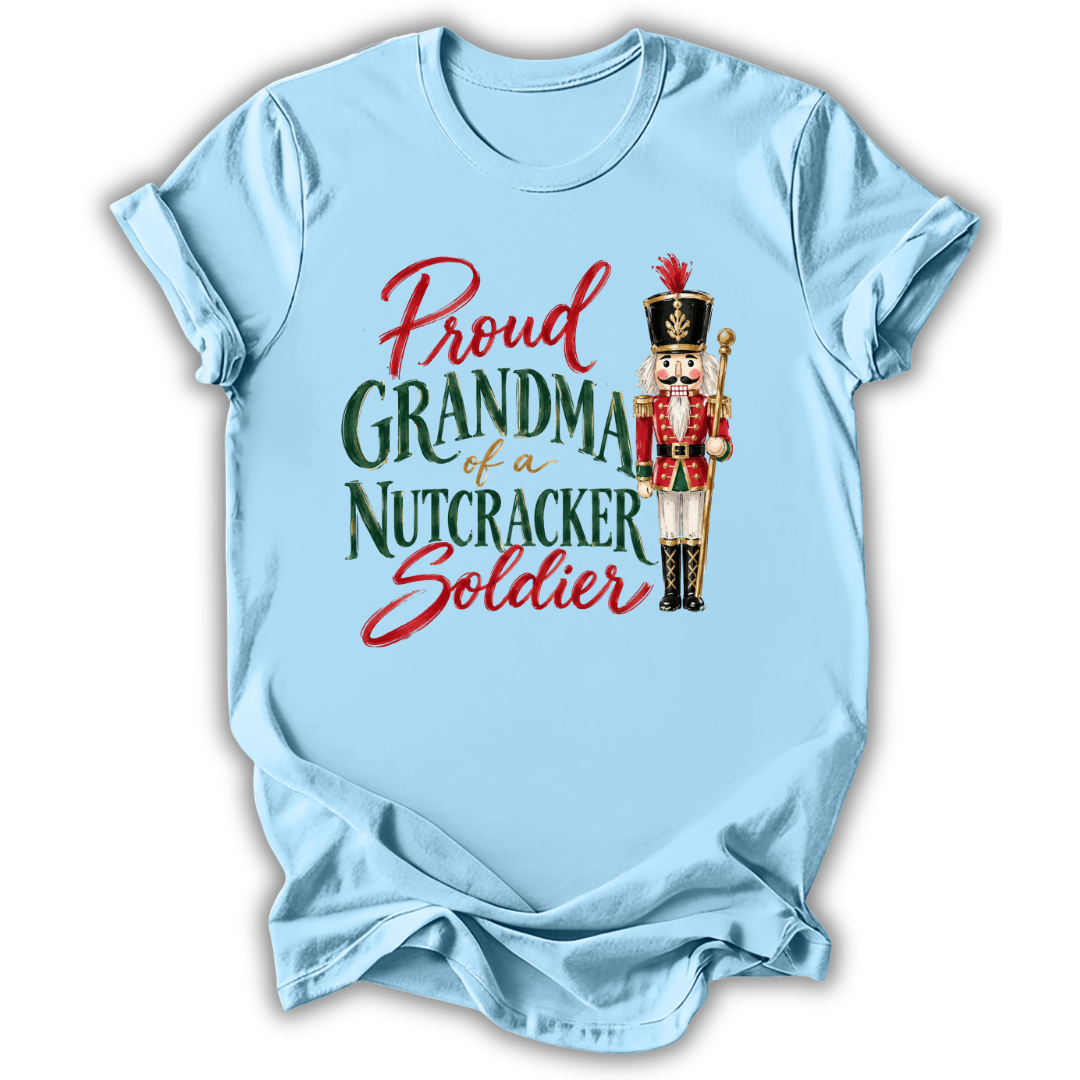 A light blue short-sleeve t-shirt with a graphic print that reads 'Proud GRANDMA of a NUTCRACKER Soldier' in red and green lettering, accompanied by an illustration of a nutcracker soldier, shown on a plain white background.