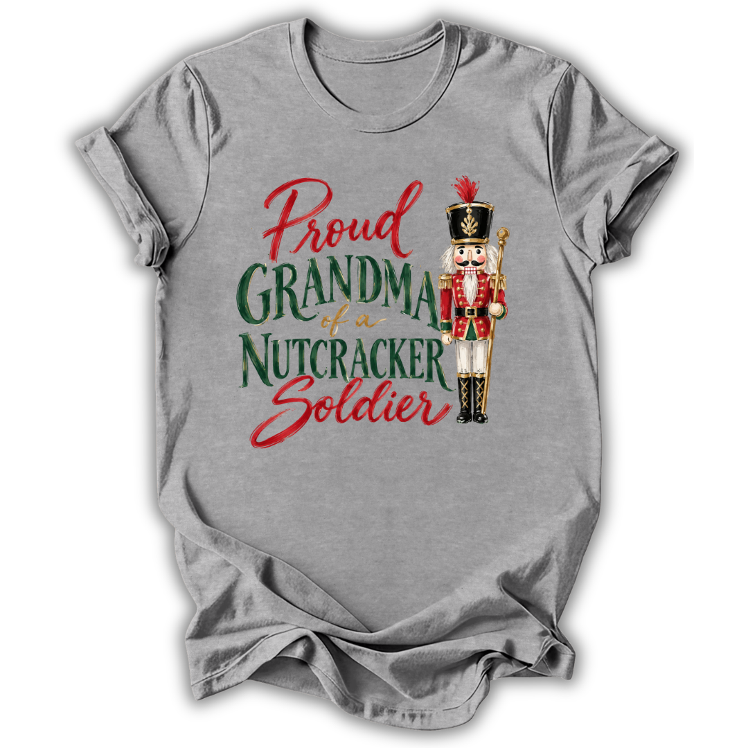 A heather gray short-sleeve t-shirt with a graphic print that reads 'Proud GRANDMA of a NUTCRACKER Soldier' in red and green lettering, accompanied by an illustration of a nutcracker soldier.