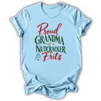 A light blue short-sleeve t-shirt with a festive graphic that reads 'Proud Grandma of a Nutcracker Fritz' in red and green lettering, displayed on a clean white background.