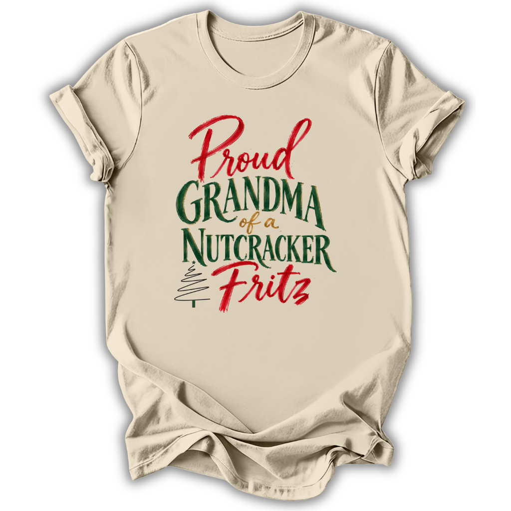 A beige short-sleeve t-shirt with a holiday-themed graphic that reads 'Proud Grandma of a Nutcracker Fritz' in red and green lettering, displayed on a clean white background.