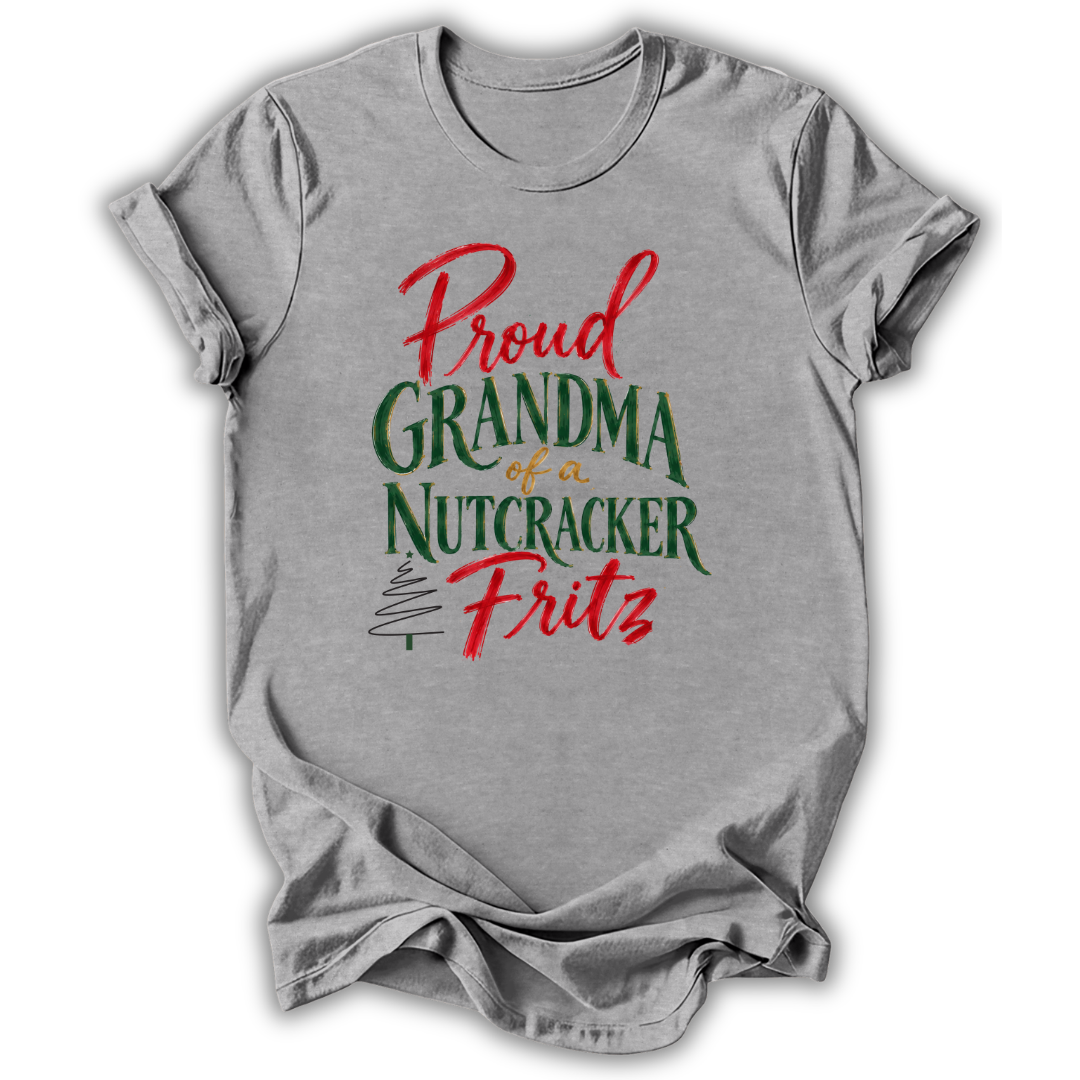 A heather gray short-sleeve t-shirt with a festive graphic on the front that reads 'Proud GRANDMA of a NUTCRACKER Fritz' in red and green lettering, displayed on a clean white background.