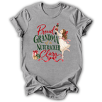 A heather gray short-sleeve t-shirt with a vintage-style Christmas graphic that reads 'Proud GRANDMA of a Nutcracker Clara' in red and green lettering, featuring an illustration of a nutcracker and a girl in a white dress.