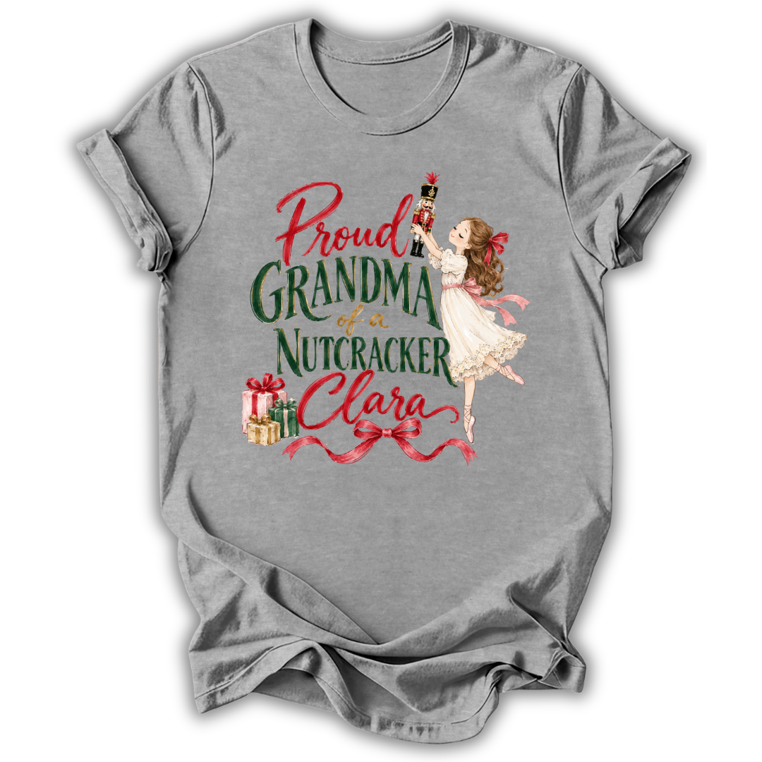A heather gray short-sleeve t-shirt with a vintage-style Christmas graphic that reads 'Proud GRANDMA of a Nutcracker Clara' in red and green lettering, featuring an illustration of a nutcracker and a girl in a white dress.