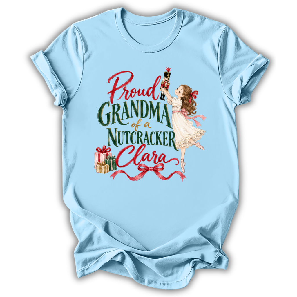 A light blue short-sleeve t-shirt with a vintage-style graphic on the front. The graphic features the text 'Proud GRANDMA of a Nutcracker Clara' in red and green lettering, accompanied by an illustration of a young girl in a white dress holding a nutcracker and some wrapped gifts.