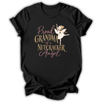 A black short-sleeve t-shirt with a graphic print that reads 'Proud GRANDMA of a NUTCRACKER Angel' in pink and gold lettering, accompanied by an illustration of a nutcracker angel ballerina, shown on a plain white background.