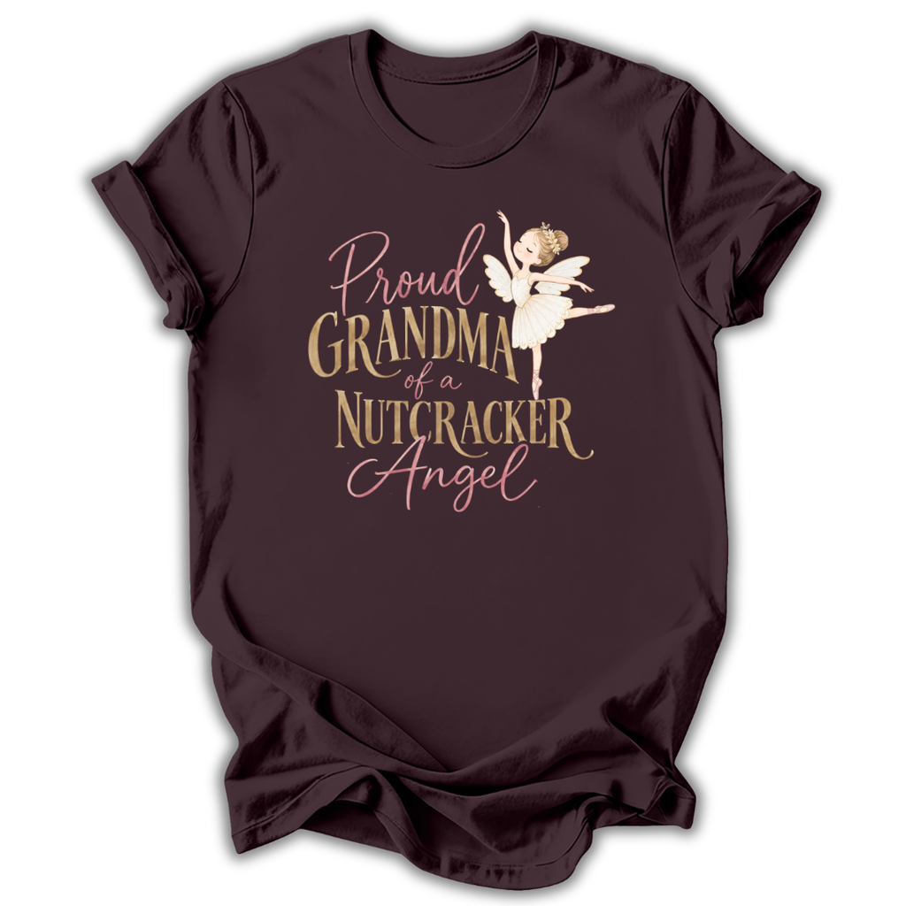 A dark plum-colored short-sleeve t-shirt with a graphic print on the front. The graphic features the text 'Proud GRANDMA of a NUTCRACKER Angel' in a mix of dusty pink and metallic gold fonts, accompanied by an illustration of a nutcracker ballerina in a white tutu.