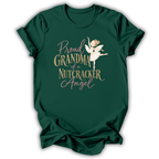 A dark green short-sleeve t-shirt with a graphic print that reads 'Proud GRANDMA of a NUTCRACKER Angel' in gold and pink lettering, featuring an illustration of a nutcracker angel in a white dress.