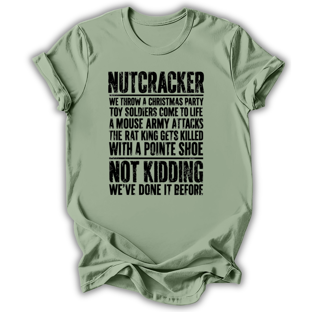 A sage green short-sleeve t-shirt with a humorous, distressed black text graphic on the front, displayed against a clean white background.