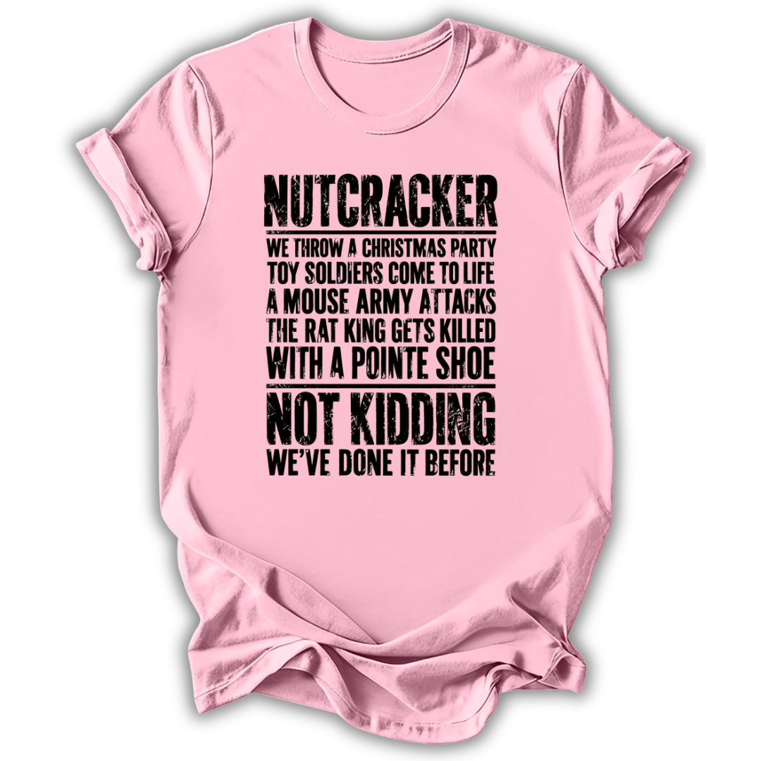 A light pink short-sleeve t-shirt with a humorous Christmas-themed text graphic printed in black distressed font on the front, displayed against a clean white background.