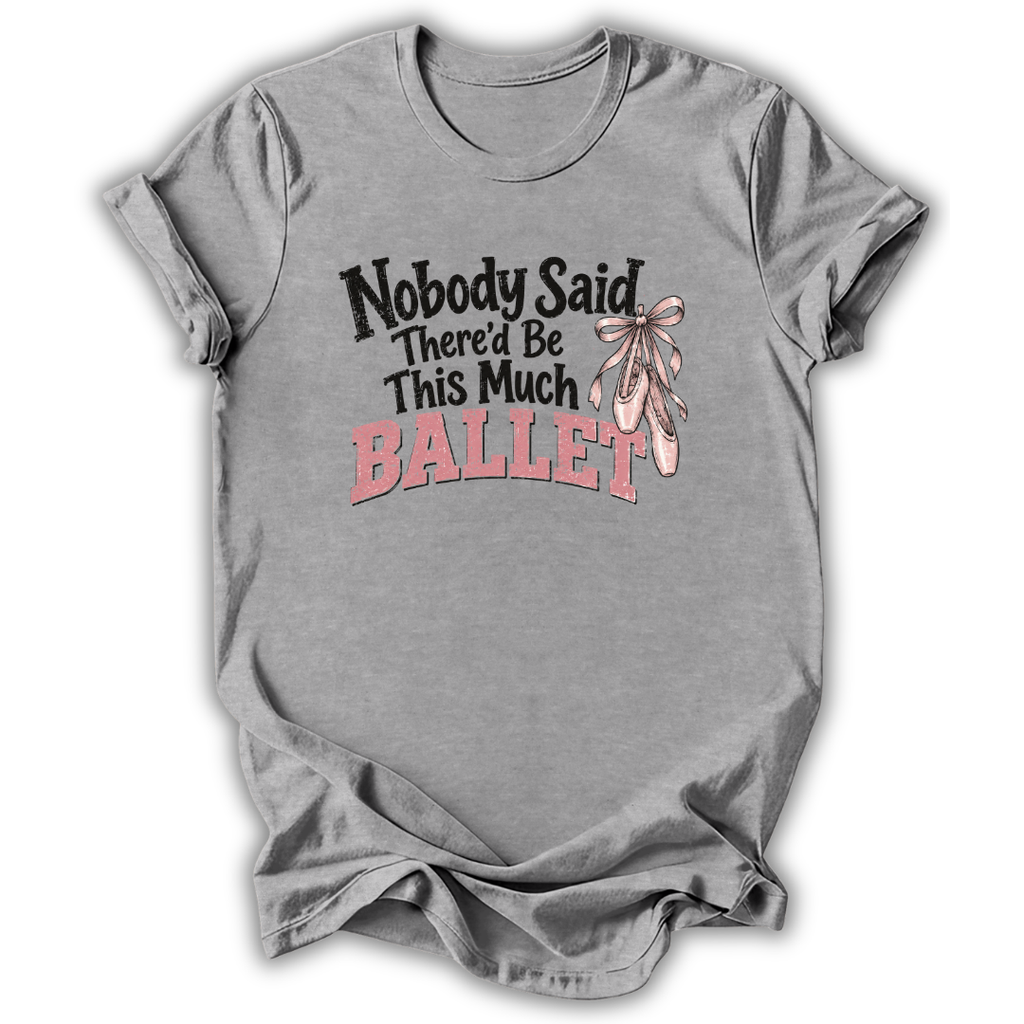A heather gray short-sleeve t-shirt with a graphic on the front that reads 'Nobody Said There'd Be This Much BALLET' in black and pink lettering, accompanied by an illustration of pink ballet slippers tied with a bow.