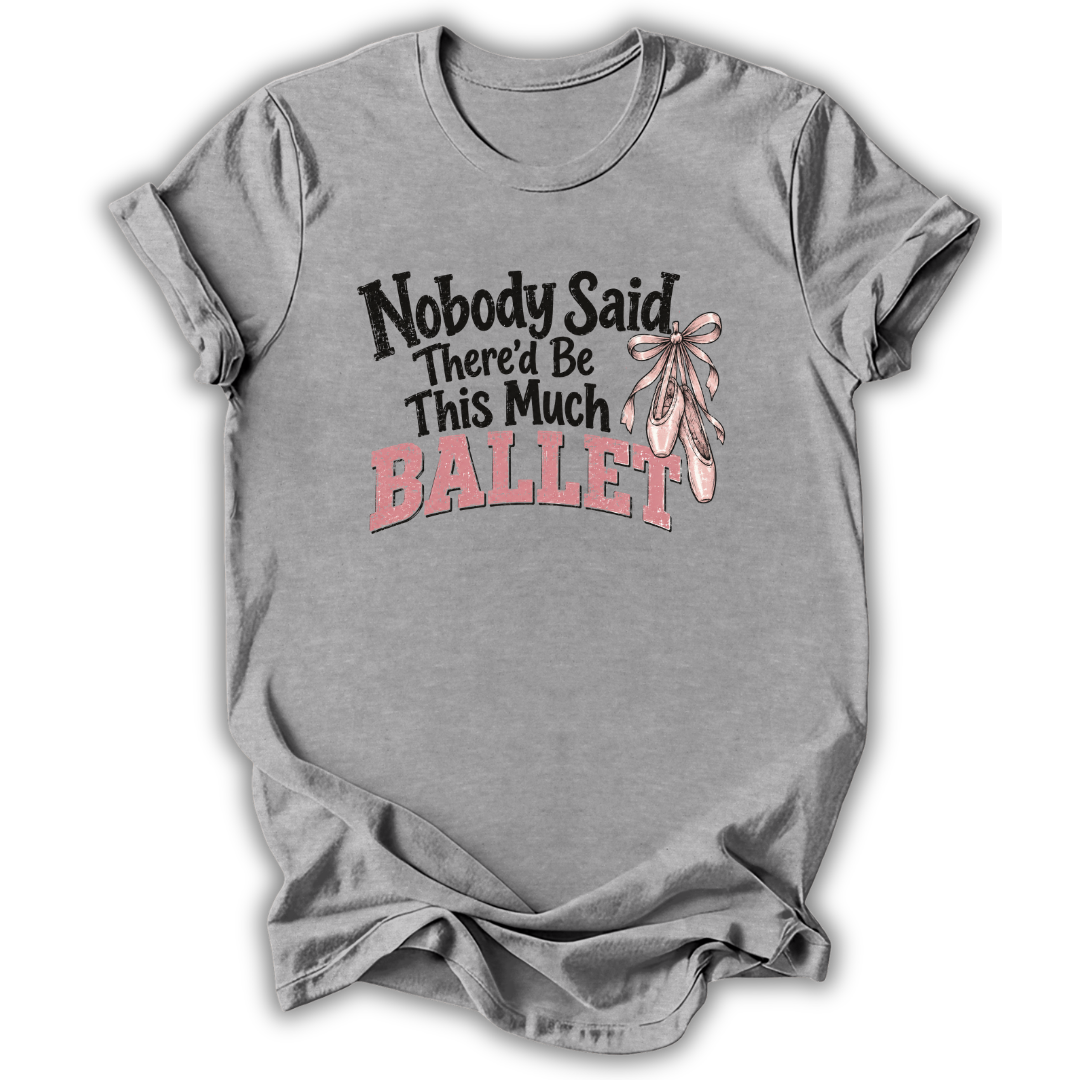 A heather gray short-sleeve t-shirt with a graphic on the front that reads 'Nobody Said There'd Be This Much BALLET' in black and pink lettering, accompanied by an illustration of pink ballet slippers tied with a bow.