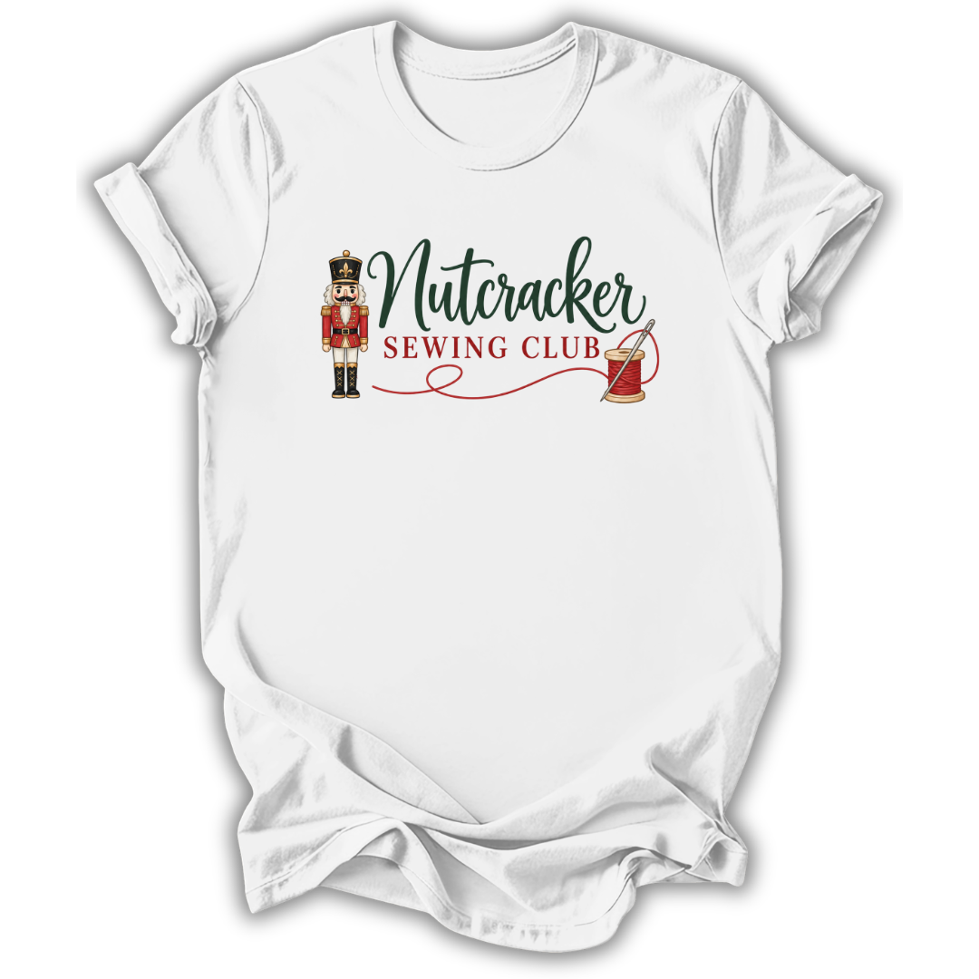A white short-sleeve crewneck t-shirt with a 'Nutcracker Sewing Club' graphic on the chest, featuring a nutcracker soldier, green script text, and red embroidery details, shown on a white background.