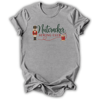 A heather gray short-sleeve t-shirt with a 'Nutcracker Sewing Club' graphic on the chest, featuring a nutcracker soldier, green script text, and a red spool of thread, shown on a white background.