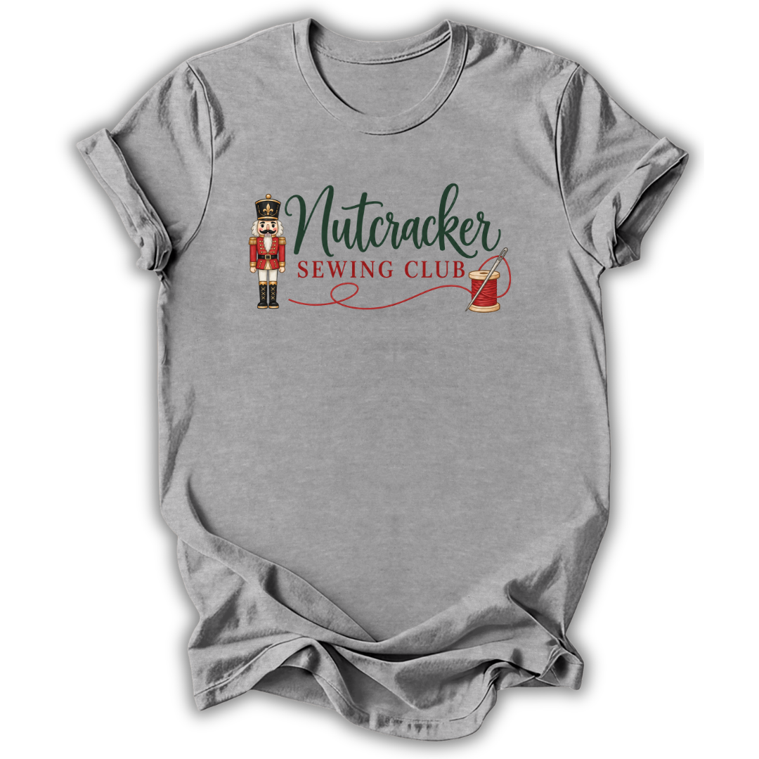 A heather gray short-sleeve t-shirt with a 'Nutcracker Sewing Club' graphic on the chest, featuring a nutcracker soldier, green script text, and a red spool of thread, shown on a white background.