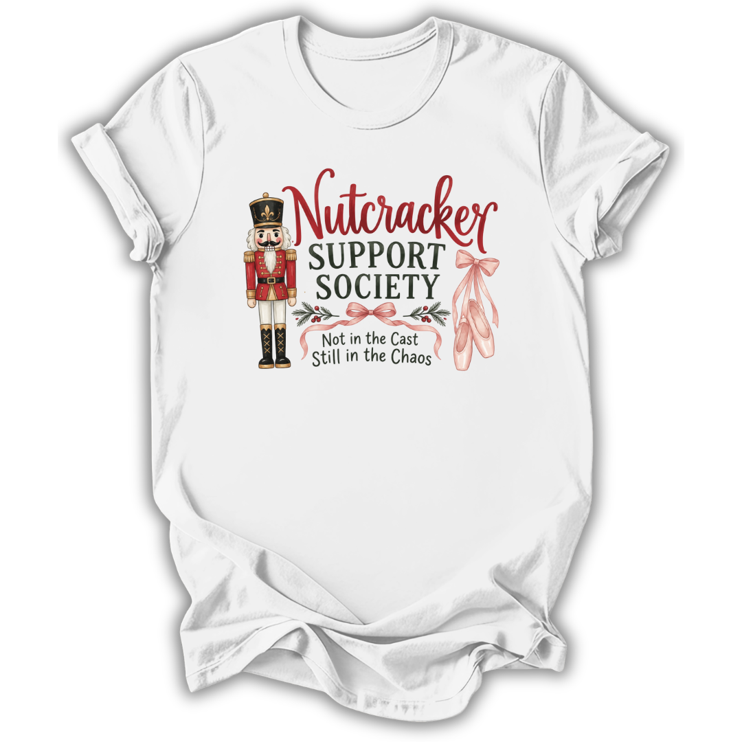 A white short-sleeve crewneck t-shirt with a graphic print on the front. The graphic features a nutcracker soldier, pink ballet slippers, and the text 'Nutcracker SUPPORT SOCIETY Not in the Cast Still in the Chaos'.